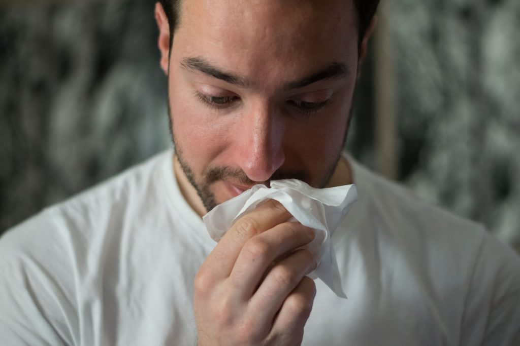 homem com gripe limpa o nariz enquanto aguarda tratamento natural com óleos essenciais